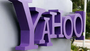灰色建築物上的紫色 Yahoo 標誌，附近有綠色植物。 — 雅虎 壁紙