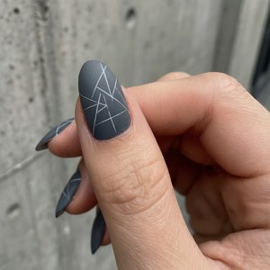 手部在混凝土背景上展示深灰色幾何指甲藝術 — Pixel Watch 壁紙
