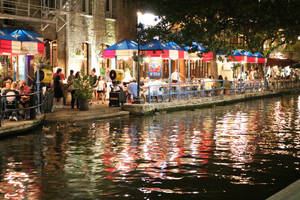 運河夜景，人們在德州旗幟遮陽傘下用餐，燈光倒映在水面上。 — 夜晚 壁紙