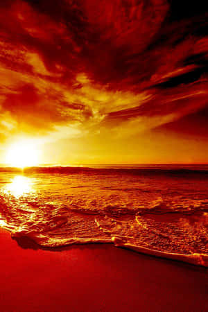 強烈的紅色和橙色夕陽映照在海浪上，沖刷著沙灘。 — 2:3 壁紙