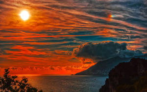 海洋上 vibrant 的夕陽，伴隨著山脈剪影和戲劇性的雲朵。 — 海灘日落 壁紙