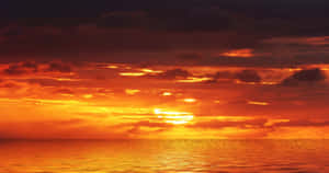 平靜海洋上鮮豔的橙色和紅色夕陽，雲朵反射著金色光芒。 — 海灘日落 壁紙