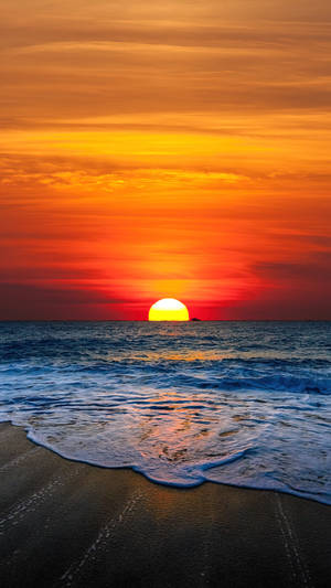 夕陽映照海洋，海浪沖刷深色沙灘。 — 日落 壁紙