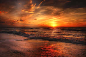 海洋上的夕陽，海浪拍打沙灘，反射出熾熱的橙色和紅色色調。 — MacBook Pro 16 壁紙