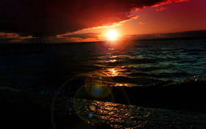 夕陽映照海面，帶有鏡頭光暈和碼頭剪影 — 日落 壁紙