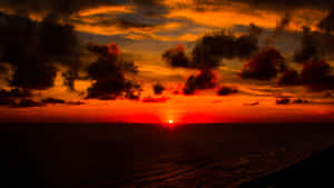 海洋上戲劇性的夕陽，熾熱的橙色和紅色雲朵在發光的地平線上形成剪影。 — 日落 壁紙