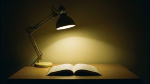 一盞檯燈照亮了黑暗房間裡木桌上的一本打開的書。 — 書桌 壁紙