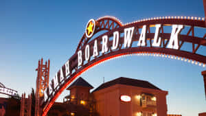 黃昏時分照亮的 Kemah Boardwalk 入口拱門，後面有建築物。 — 德克薩斯州旗 壁紙