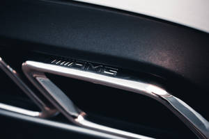 黑色汽車內飾飾板上的鍍鉻AMG標誌，帶有金屬光澤。 — Mercedes-Benz 壁紙