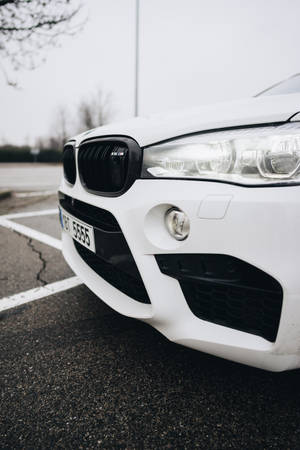 白色BMW X5 M停泊在瀝青停車場，天空多雲。 — F1 iPhone 壁紙