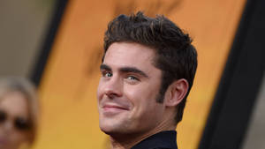 一名男子在橙色和黑色背景的活動中微笑。 — 柴克·艾弗隆 壁紙