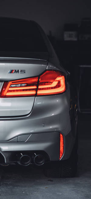 銀色BMW M5後視圖，在黑暗車庫中亮起的尾燈和雙排氣管。 — Galaxy S24 FE 壁紙