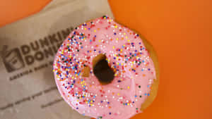 粉紅糖霜甜甜圈配彩色糖粒放在Dunkin' Donuts袋上，橙色背景 — Dunkin Donuts 壁紙