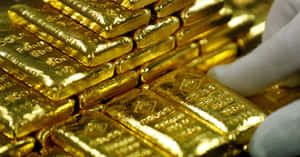 戴著手套的手觸摸一堆閃閃發光的金條。 — 金色亮片 壁紙
