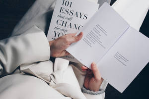 穿著白色浴袍的人正在閱讀一本名為101 Essays that will Change the Way You Think的書。