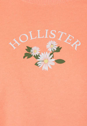 珊瑚粉紅色毛衣，帶有白色雛菊花卉圖案和 Hollister 品牌標誌。 — OnePlus Pad 3 壁紙