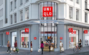 人們走過帶有紅色標誌和玻璃窗的 Uniqlo 服裝店。 — 16:10 壁紙