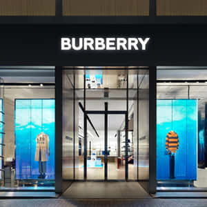 Burberry商店正面，設有玻璃門和顯示服裝的藍色數位顯示螢幕。 — Burberry 壁紙