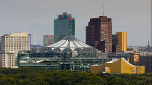 城市天際線，前景有現代玻璃建築和綠色樹木。 — 柏林 壁紙