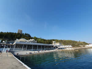人們在現代海邊亭閣附近放鬆，享受藍色海水和晴朗天空。 — 海景 壁紙