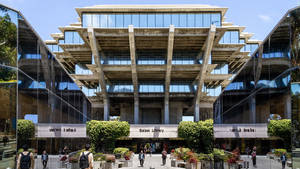 學生在現代混凝土和玻璃圖書館建築附近行走，該建築設有分層陽台。 — 加州 壁紙