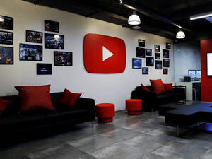 YouTube 辦公室休息區，配有黑色沙發、紅色靠墊，牆上有大標誌。 — 客廳 壁紙