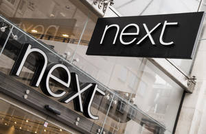 玻璃店面上的黑白「next」商店標誌，帶有城市倒影。 — 購物 壁紙