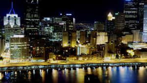 夜晚城市天際線，發光的建築物倒映在河流中。 — 城市景觀 壁紙