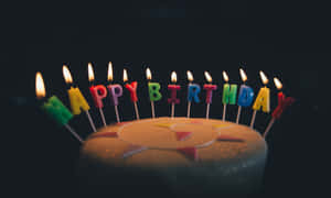 一個生日蛋糕，上面有點燃的蠟燭，用彩色字母拼出 happy birthday。 — 生日快樂蛋糕 壁紙