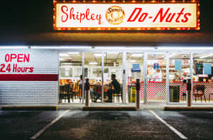 夜間亮燈的24小時Shipley Do-Nuts餐廳，裡面有人坐著。 — 購物 壁紙