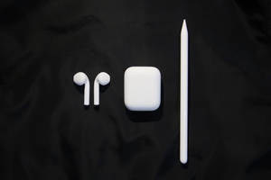 白色 Apple AirPods 耳機保護殼和觸控筆，置於黑色布料上。 — AirPods 壁紙