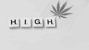 灰色背景上，Scrabble 字母磚拼出 HIGH，旁邊有一片大麻葉。 — 簡約暗黑美學 壁紙