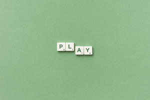 白色 Scrabble 字母磚在綠色背景上拼出 play