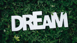 白色3D字母拼出DREAM，置於綠色葉子背景上。 — 夢幻 GIF 壁紙