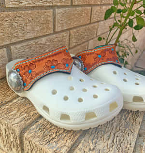 白色Crocs鞋，帶有裝飾性皮帶和綠松石，放在石面上。 — Galaxy Z Flip7 FE 壁紙