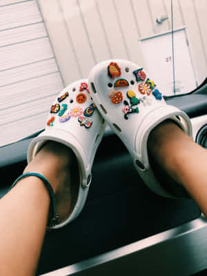 穿著白色Crocs鞋的腳，鞋上帶有彩色飾物，擱在汽車儀表板上。 — Crocs 壁紙