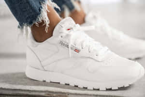 白色Reebok運動鞋與磨邊牛仔褲在混凝土上。 — 銳步 壁紙