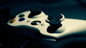白色Xbox 360遊戲控制器，在昏暗的藍光下帶有彩色按鈕。 — 4K 遊戲 壁紙