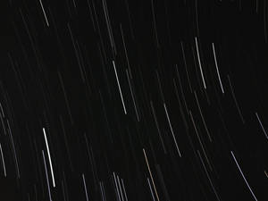 星軌在黑暗的夜空中劃出弧線的長時間曝光照片。 — 黑色桌面 壁紙