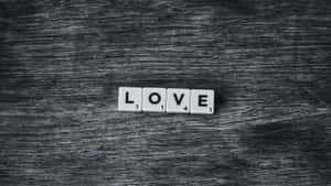 白色拼字磚在深色木質背景上拼出 love — 簡約暗黑美學 壁紙
