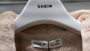 白色衣架上的米色絨毛衣物，附有SHEIN品牌標籤和尺寸標籤。 — 美學粉色GIF 壁紙
