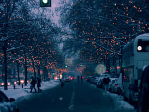 積雪的城市街道，樹上掛著發光的紅燈，夜晚行人漫步。 — 聖誕燈飾 壁紙