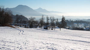 白雪覆蓋的山坡，腳印通向霧氣瀰漫的村莊和遠山。 — 冬季風景 壁紙
