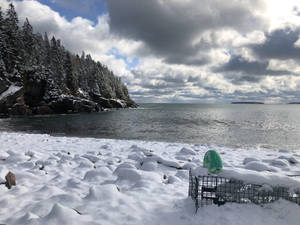 白雪覆蓋的海灘，龍蝦籠和綠色浮標靠近岩石海岸。 — 雲朵美學 壁紙