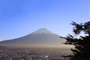 白雪覆蓋的富士山俯瞰著小鎮，前景有秋天的樹木，夕陽西下。 — 富士山 壁紙