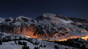 星空下白雪覆蓋的山峰，夜晚山谷燈光閃爍。 — 山脈 壁紙