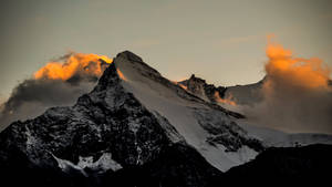 暮色中白雪覆蓋的山峰，金色雲彩在其輪廓周圍發光。 — 地形 壁紙