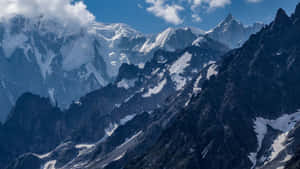 白雪皚皚的山峰在明亮的藍天下，從深色的岩石地形中拔地而起。 — 酷寒冬季 壁紙