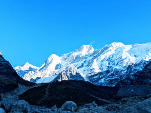 晴朗藍天下的雪山山脈，岩石前景 — 曼達洛人 壁紙