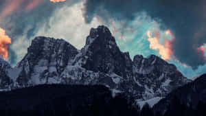 在多彩的黃昏雲層下，白雪覆蓋的山脈，下方是黑暗的森林。 — 山脈 壁紙